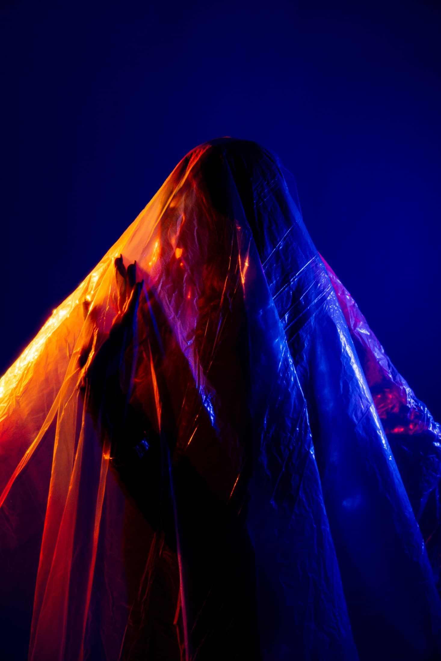 A veiled figure illuminated in saturated blue and amber light.