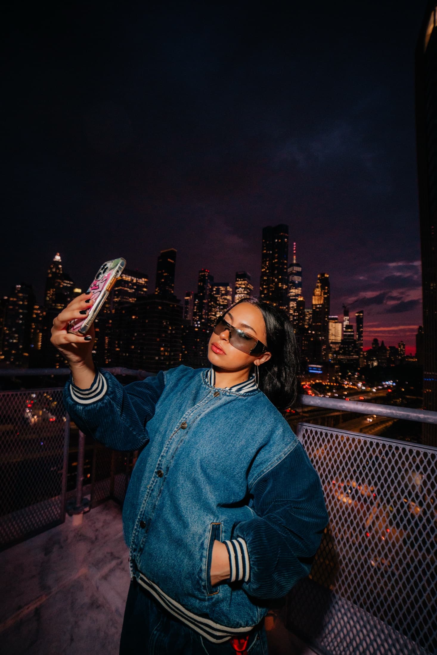 A flash-lit portrait on a rooftop with a city skyline at night.