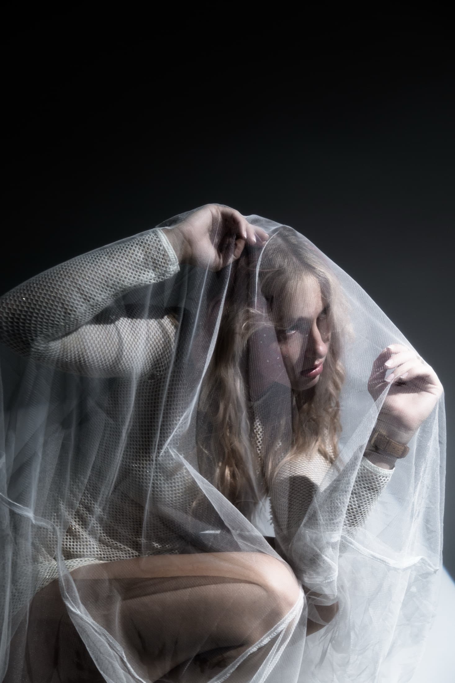A seated figure wrapped in layers of sheer white fabric.